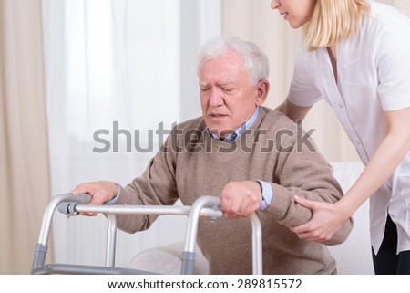 Careful nurse helping senior man with walker to stand up