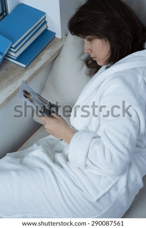 Depressed woman lying in bed and holding ex-boyfriend\'s photo