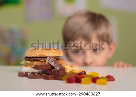 Greedy little boy looking at unhealthy tasty snacks