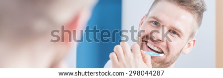 Smiling attractive man brushing teeth in front of mirror
