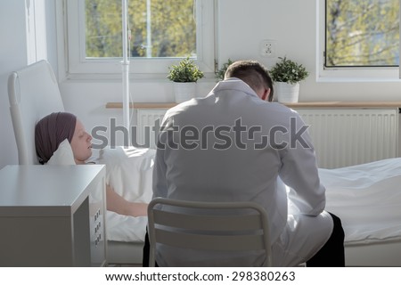 Worried doctor sitting by his sick patient in hospital