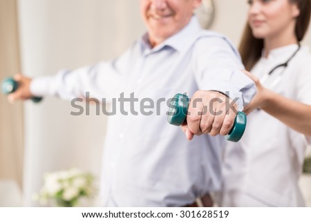 Retiree training with dumbbells assisted by young physiotherapist