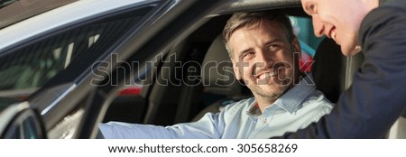 Happy man sitting in the car and smiling to his friend