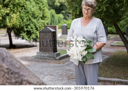 Photo of mature woman on cemetery holding white lilies