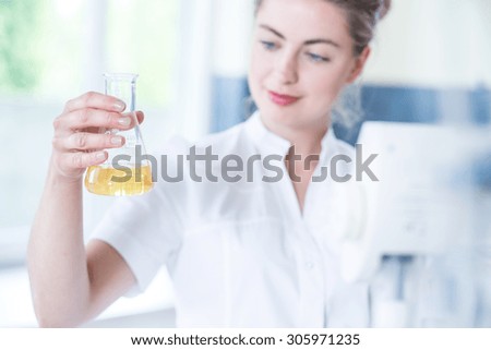 Worker of laboratory holding flask with yellow fluid