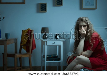 Nervous girl sitting on the bed and biting nails