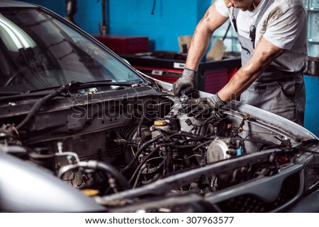 Picture of uniformed auto mechanic maintaining car engine