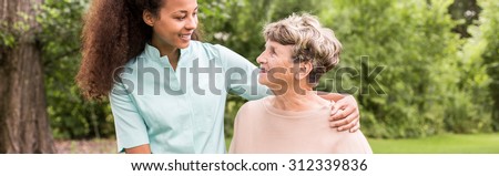 Panorama of young female afroamerican caregiver supporting elderly woman