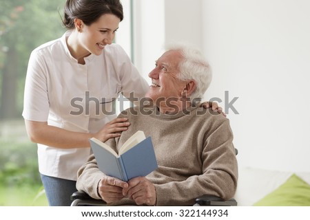 Photo of elderly man reading book and his private nurse