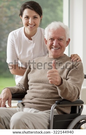 Picture of smiling old man sitting on wheelchair and carer