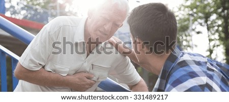 Caring young man helping sick old man on a street