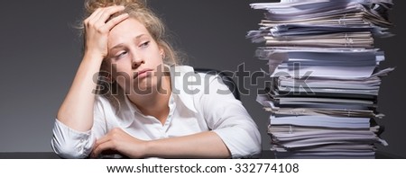 Tired  young woman at work and stack of paperwork