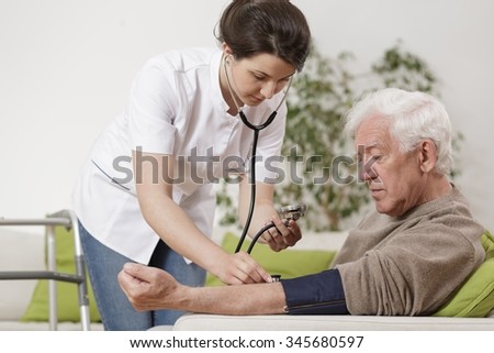 Young nurse taking old man\'s blood pressure