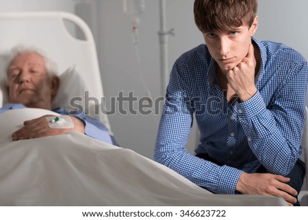 Sad grandson at his grandfather\'s bed in hospital