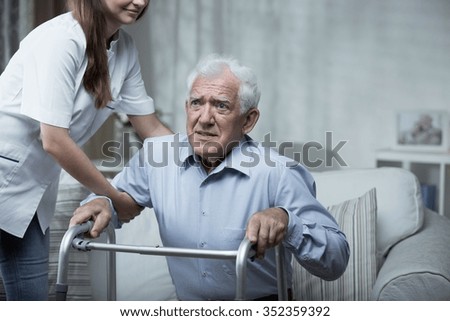 Disabled man using a walking frame with help of the nurse