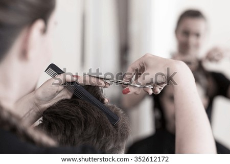 Female hair stylist cutting man\'s hair with scissors