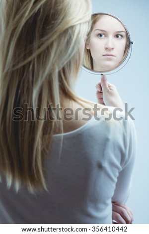 Young pretty girl looking at her reflection in mirror