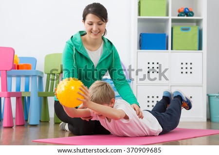 Boy exercising with small gym ball and his smiling instructor