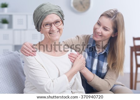 Smiling cancer woman with headscarf embraced by young happy girl