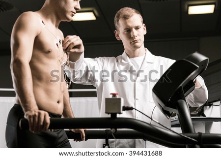 Sportsman standing on treadmill during medical examination and doctor in white uniform