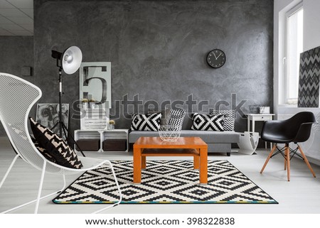 Trendy, grey living room with sofa, chairs, standing lamp, wood coffee-table and pattern decorations in black and white