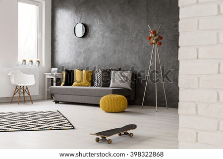 Grey interior with sofa, chair, yellow details and pattern decorations in black and white, skateboard lying on the floor