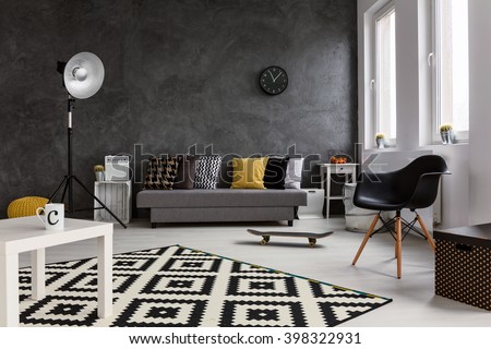 Grey living room with sofa, chair, standing lamp, small white table and black and white pattern carpet