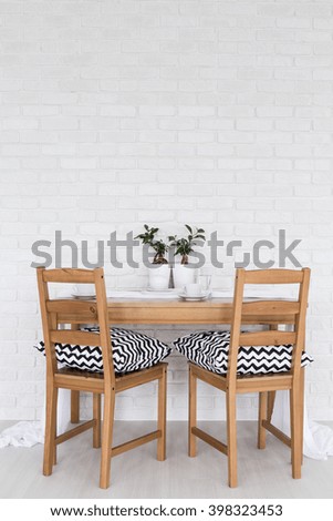 Simple wood table and two chairs standing in light interior with decorative brick wall
