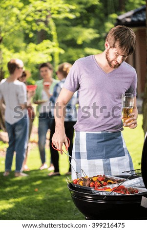 Man preparing food on garden barbecue with friends