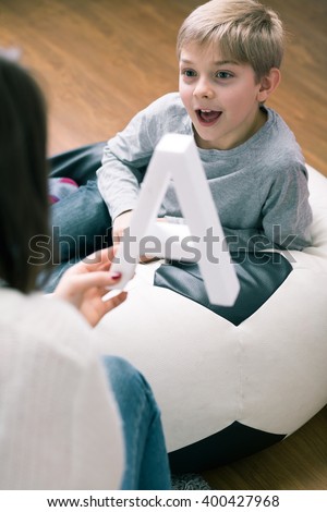 Pedagogue helping little boy to learn new letters. Woman holding big letter a and happy boy next to her