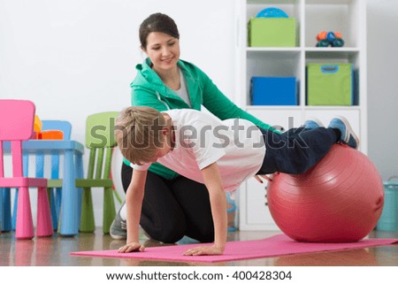 Boy during physiotherapy exercises on gym ball and woman instructor.