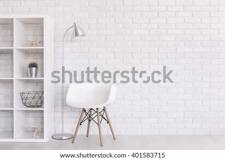 White regale with home decorations, standing lamp and modern chair standing in light room with brick wall design
