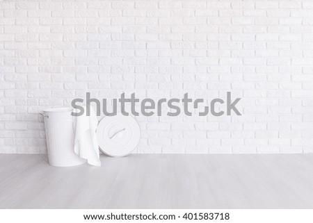 White laundry basket standing in spacious room with light flooring and brick wall