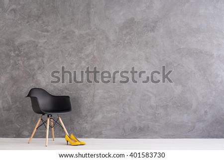 New black chair and yellow high heels standing in spacious interior with cement wall design