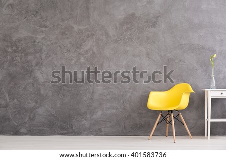 New yellow chair and small, decorative table standing in interior with grey wall
