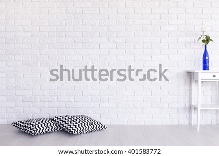 Decorative, black and white pattern pillows and small table standing in white interior with brick wall design