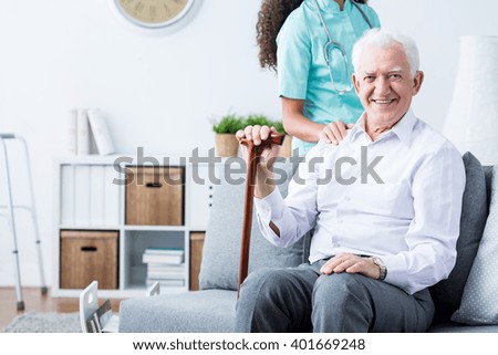 Happy senior disabled man with walking stick and caring young nurse