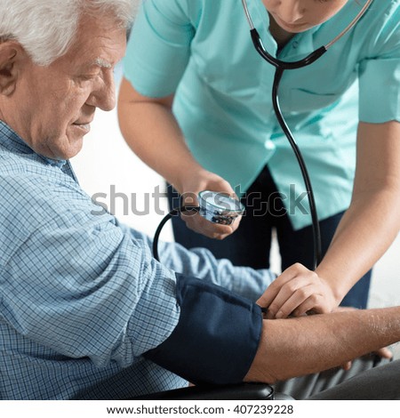 Young attractive nurse checking the elderly man\'s hypertension