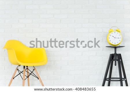 Light interior with yellow chair, small table and trendy alarm clock, brick wall in the background