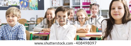 Panorama of a classroom in primary school with rows of smiling pupils sitting at their desks