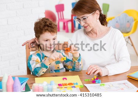Little happy boy having classes with occupational therapist. Setting words from colorful letters