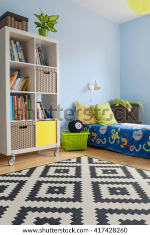Corner of a blue teenager room with large rack on wheels, covered bed and patterned carpet