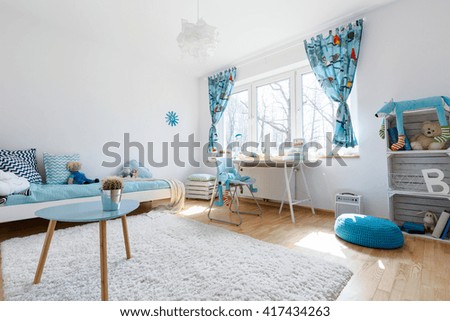 Very spacious and light child room with large window, filled with white and blue decorative elements