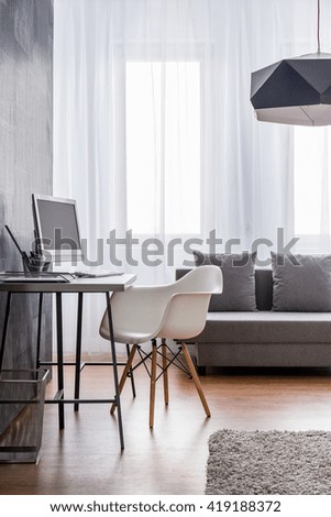 Minimalist workspace with grey desk and white designer chair arranged as a part of a very bright living room