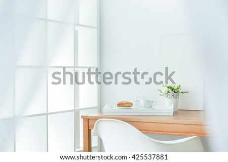 Wooden dining table in the corner of room. On it white tray with puff pastry and coffee