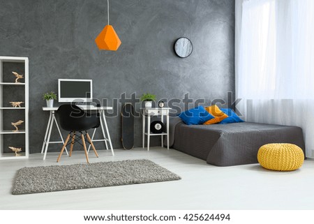 Cozy stylish bedroom designed for teenage boy. Grey walls and wooden floor. On the wall skate board and shelf with wooden models