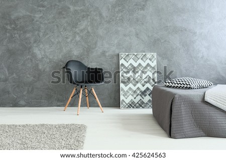 Modest stylish bedroom with bed and chair. Grey walls and wooden floor