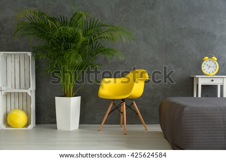 Modern designed bedroom with grey walls. Yellow chair next to green plant and white shelf made of boxes
