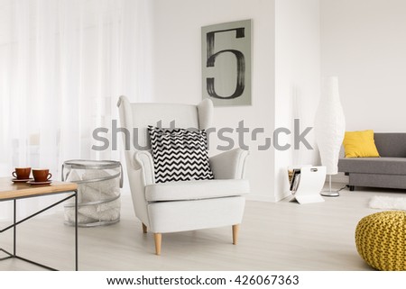 Light living room with simple table and comfortable armchair with decorative pattern pillow