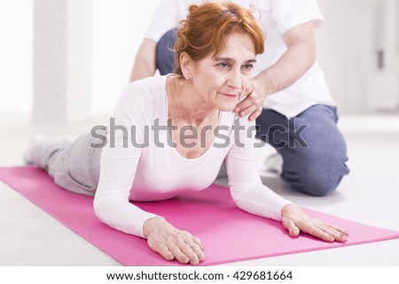 Elderly woman after injury stretching her spinal during rehabilitation. Next to her physical therapist helping with exercise